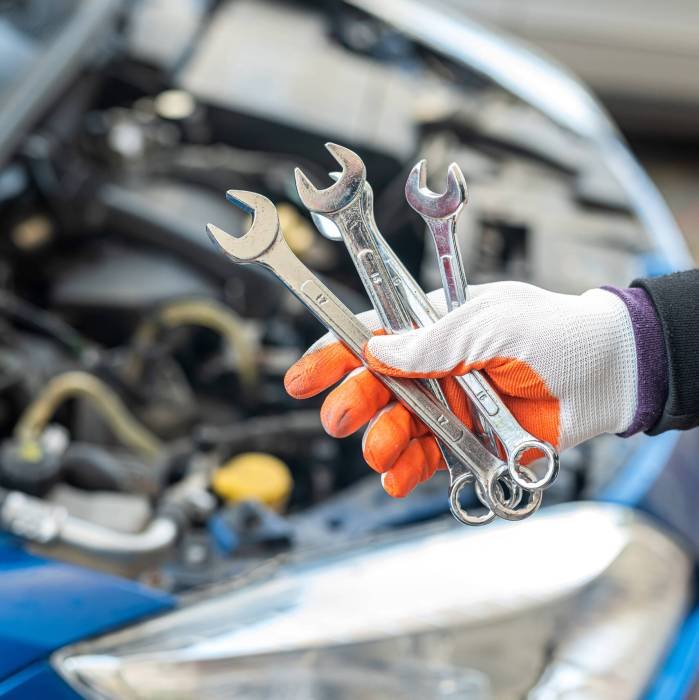 Man’s gloved mechanic’s hand holds car tools near a painted car with an open hood Man's gloved mechanic's hand holds car tools near a painted car with an open hood. Tools concept. Car repair concept